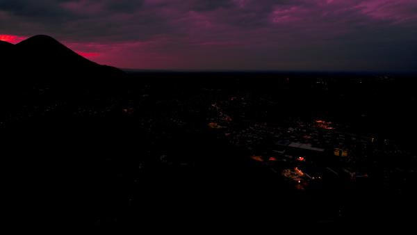 City skyline under a dark, ominous purple sky at dusk, with city lights starting to illuminate.
