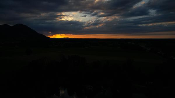 Vibrant sunset peeking through dark silhouettes of mountains and clouds.