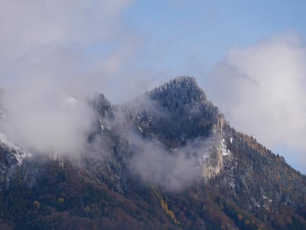 Snow-capped mountain peak shrouded in mist with a partially cloudy sky.