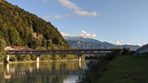 Wooden bridge crossing a calm river with mountains in the distance.