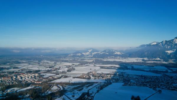 Aerial view of snow-covered fields with a dense bed of clouds between mountain ranges.
