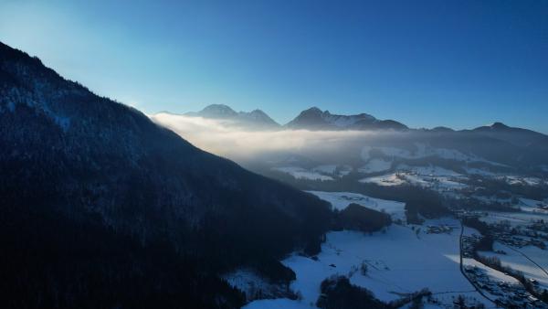 Sunlight breaking through the misty clouds over snowy mountains at dawn.
