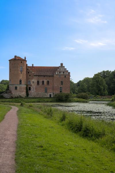 A castle with a little pond in the foreground and blue sky with some clouds in the background.