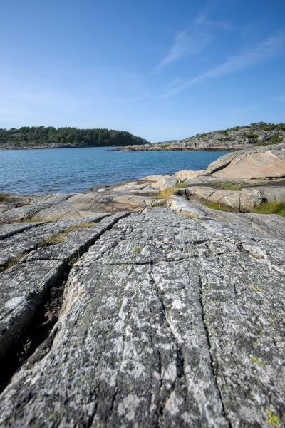 There is a large area of rocks in the foreground of the image. Behind that there is the sea and following two land masses. One is a island and the other mainland. The sky is blue with next to no clouds.