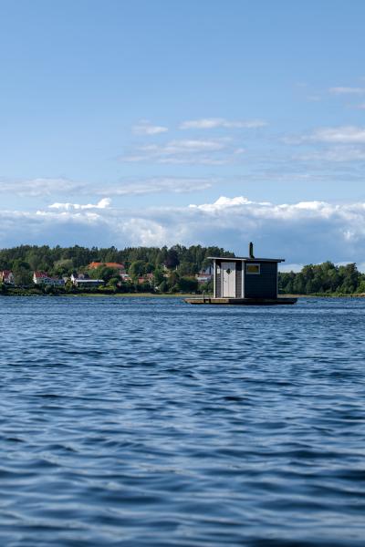A swimmen sauna on a swedish lake. In the background there are some trees and houses.