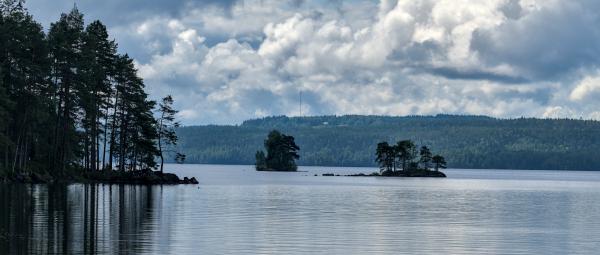 A landscape image of a lake with some small islands on it. In the background there is a forest.
