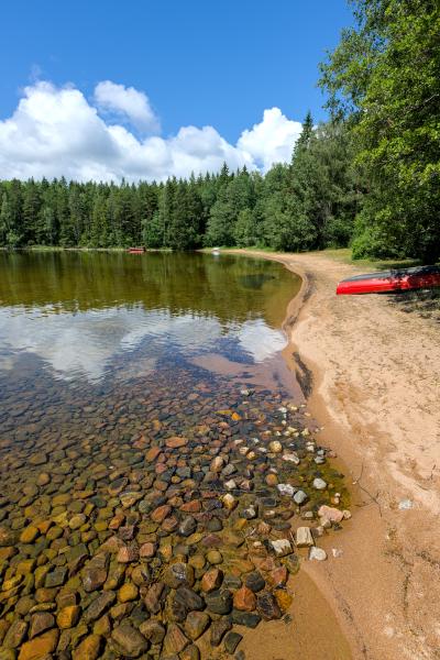 Photograph of a sandy beach of a lake. You can clearly see the stones in the shallow water. On the beach there are lying several boats.