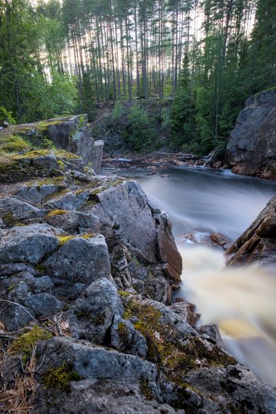 A waterfall with a forest in the background. The water is washed out because of the long exposure. The sky is blue and cloudy.