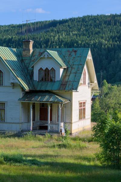 A old house with little meadow / garden in front of it and the forest in the background.