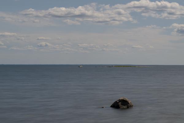 A small rock in a washed out sea with a small island in the background and a large one at the horizon.
