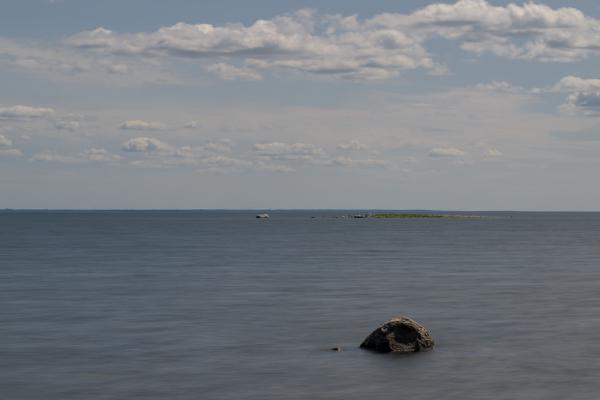 A small rock in a washed out sea with a small island in the background and a large one at the horizon.
