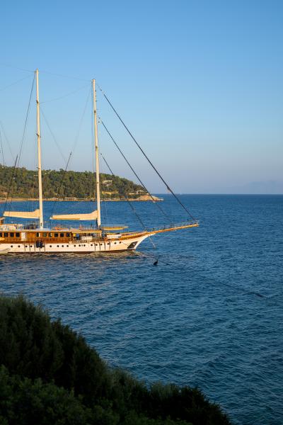A sail ship with no sails up. It is docked to land and reflecting the colors of a distant sunset.