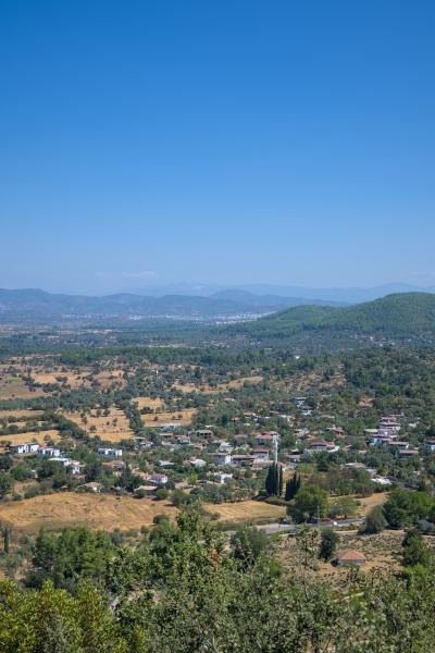 A photograph of a turkish village between some green hills. There are also a few trees in the image.