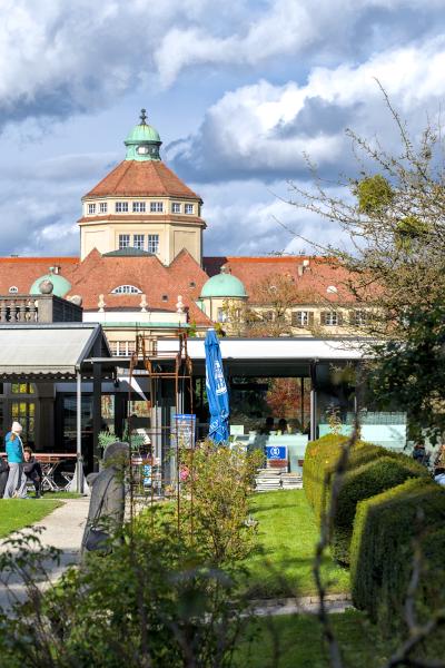 An old looking building with some green bushes and roses next to the way to the building. In the background there are white clouds.