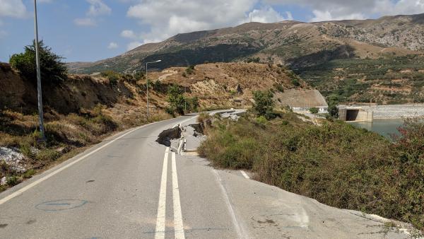 Damaged street with a landslide, showing broken asphalt and a view of a reservoir.