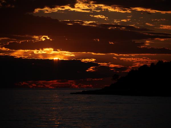 The sky glows with radiant hues of orange and yellow as the sun sets behind clouds.