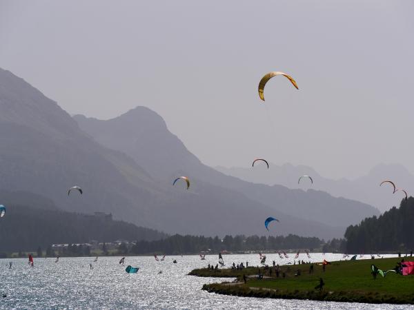 Colorful kitesurfing sails dotting the lake with mountains in the backdrop.
