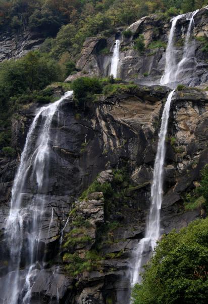 Multi-tiered waterfall cascading down rugged cliffs, embraced by lush vegetation.