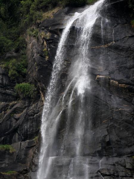Multi-tiered waterfall cascading down rugged cliffs, embraced by lush vegetation.
