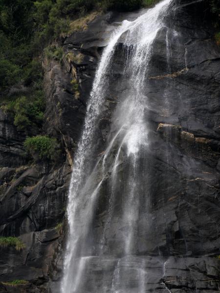 Multi-tiered waterfall cascading down rugged cliffs, embraced by lush vegetation.