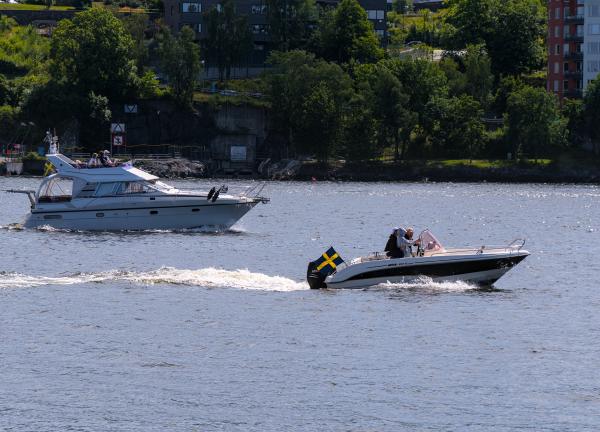 Photo of a motor boat and a small yacht in the sea around Stockholm. In the background are trees, buildings and streets.