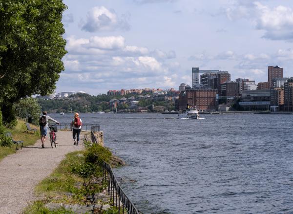 A photo taken in Stockholm showing a gravel way on the left and the sea on the right. On the sea you can see a ship. On the right side in the background you can see a few large houses.