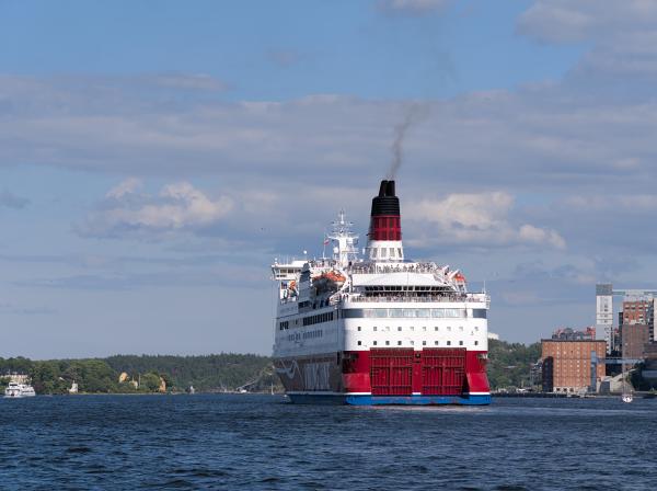 Some sort of ferry ship leaving from Stockholm. You can see a few island of the archipelago in the background. The sky is blue with a few clouds.