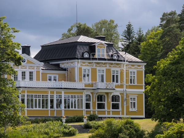 A nobel looking swedish house and a few trees framing it. The house looks pretty large.