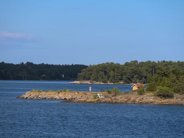 You can see two islands of the Stockholm archipelago and the sea in this photo. Above this scene is a blue sky.