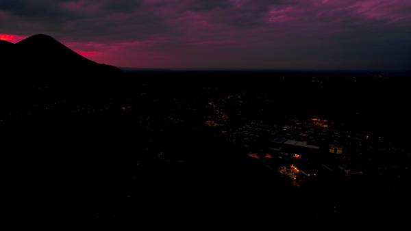 City skyline under a dark, ominous purple sky at dusk, with city lights starting to illuminate.