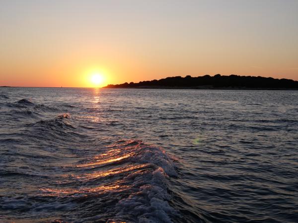 Waves of the sea glimmering under the orange hues of the setting sun, near a coastline.