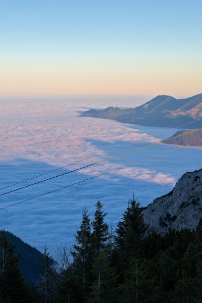 This image is photographed from above the clouds. You are looking down on them from a mountain. There can be seen another mountain in the image. The sky is light blue / orange.