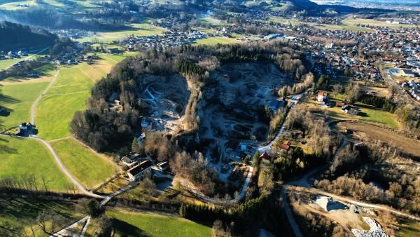 En flygvy över ett stort stenbrott som skurits ner i marken, omgivet av kal vinterskog, med en stad av rödtakade hus, ängar och vägar ända inpå kanten.
