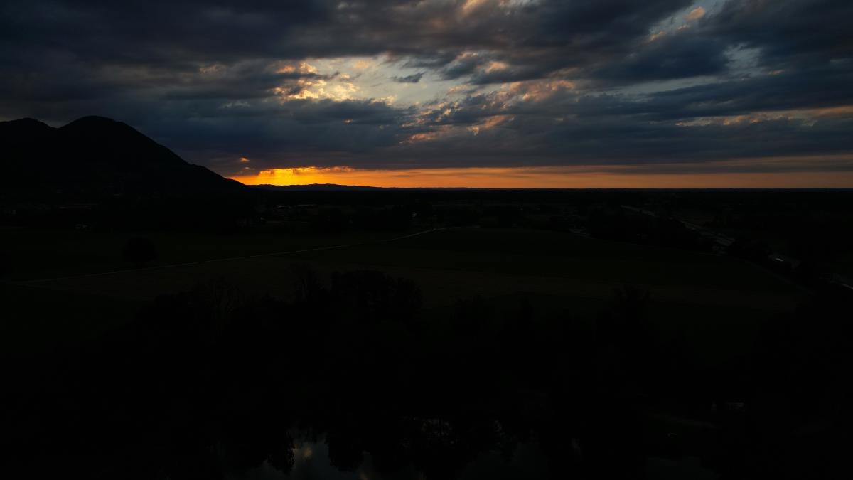 En lysande solnedgång som tittar fram genom mörka siluetter av berg och moln.
