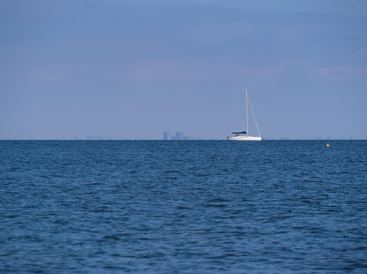 Ein Schiff, das im Öresund fährt, mit der Skyline von Kopenhagen im Hintergrund. Der Himmel ist leicht blau.