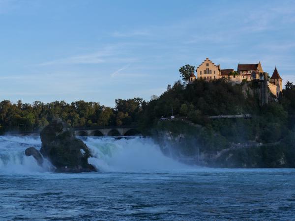 Foto des Rheinfalls in der Schweiz. Im Hintergrund ist ein altes Gebäude zu finden.