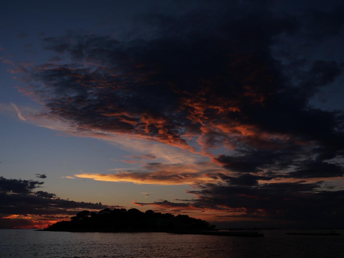 Die Silhouette einer Insel vor einem Sonnenuntergangshimmel mit leuchtenden Wolken über dem Meer.