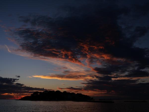 Die Silhouette einer Insel vor einem Sonnenuntergangshimmel mit leuchtenden Wolken über dem Meer.