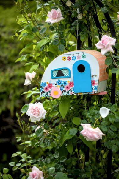 Ein Vogelhaus in Form eines Wohnwagens, das in einem Rosenbusch hängt.