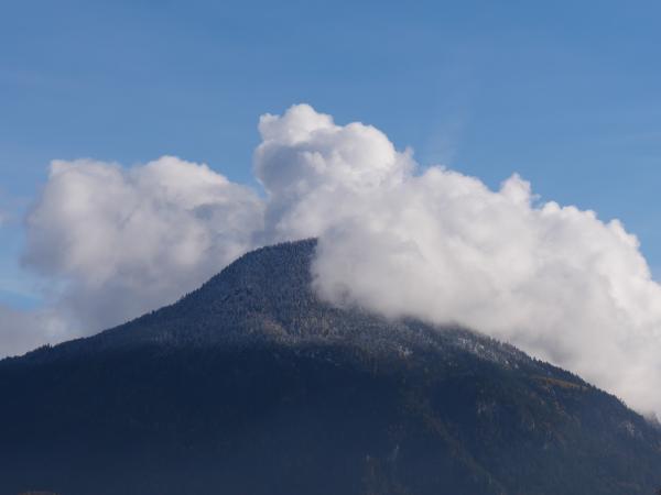 Ein Berggipfel unter einem klaren blauen Himmel mit flauschigen Wolken.