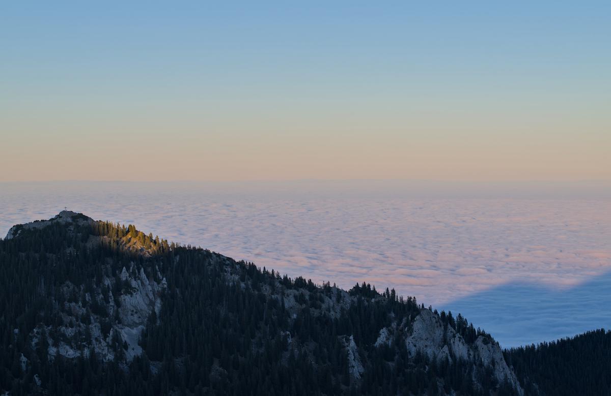 A mountain above an infinite looking sea of clouds. The sky looks very soft with a tone of blue and orange.