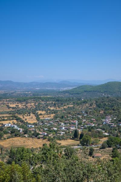 A photograph of a Turkish village between some green hills. There are also a few trees in the image.