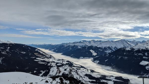 Panoramic view of the snow-capped Alps with clouds below the mountain peaks.