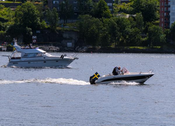 Photo of a motor boat and a small yacht in the sea around Stockholm. In the background are trees, buildings and streets.