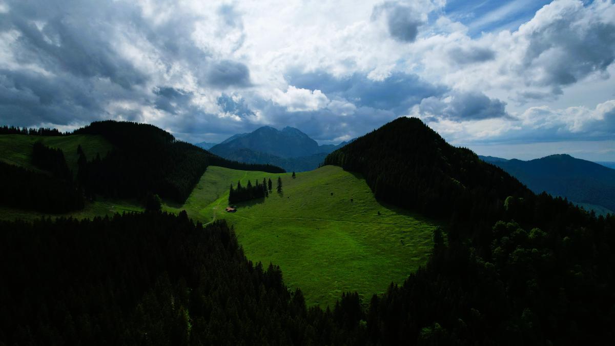 Luftaufnahme eines saftig grünen Tals mit den Bergen Rehleitenkopf und Riesenkopf im Hintergrund.