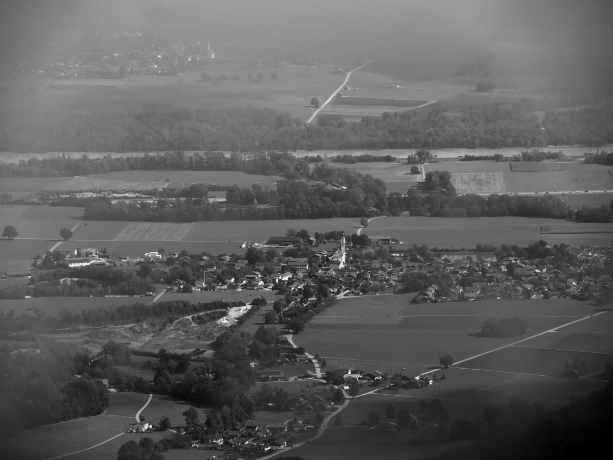 A black and white image of a small village in Bavaria, Germany. The image was taken through the fog from a mountain. Behind the village in the background a river and another village can be seen.