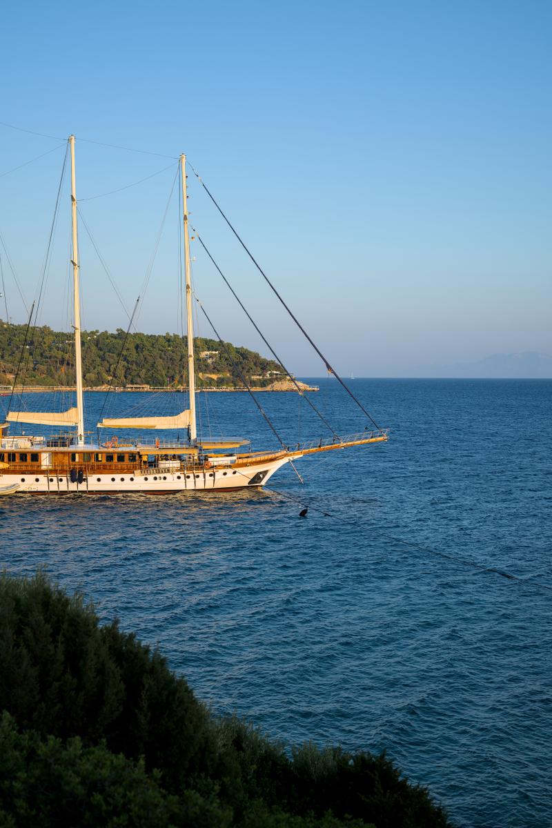 Ein Segelschiff mit eingeholten Segeln. Es liegt am Ufer vertäut und spiegelt die Farben eines fernen Sonnenuntergangs wider.
