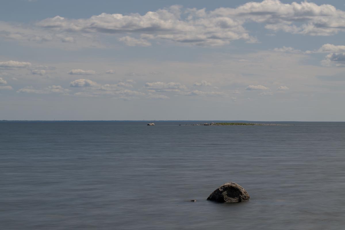 Ein kleiner Felsen in einem verwaschenen Meer, mit einer kleinen Insel im Hintergrund und einer großen am Horizont.