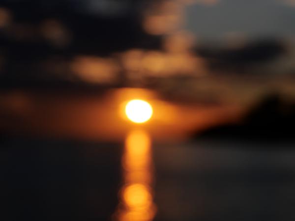 Die Sonne geht über dem Meer unter, ihr Licht spiegelt sich im Wasser, und der Horizont zeichnet sich in Silhouetten ab.