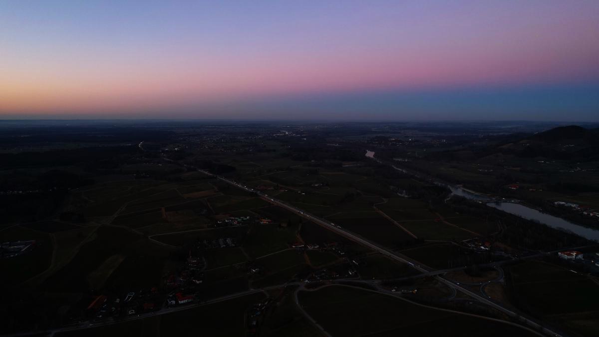 Luftaufnahme eines bayerischen Dorfes in der Dämmerung, mit Bergen im Hintergrund und einem schwach erleuchteten Himmel.
